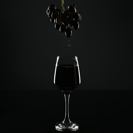 Glass of red wine and grapes with drops on black backgroundの写真素材