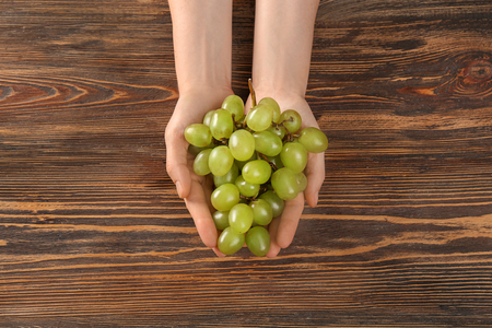 Woman holding fresh ripe grapes on wooden backgroundの写真素材