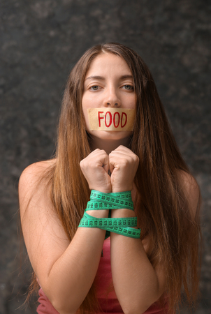 Tied young woman with measuring tape and plastered mouth on grey background. Diet conceptの写真素材