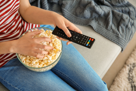 Young woman eating popcorn while watching TV at home, closeupの写真素材
