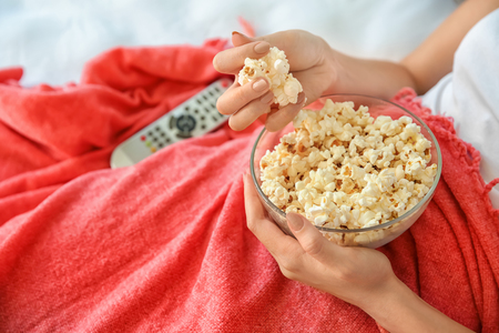Young woman eating popcorn while watching TV in bedroom, closeupの写真素材