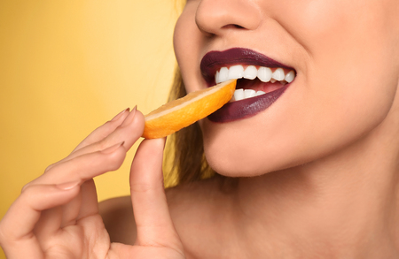 Beautiful young woman with dark lipstick and lemon slice on color background, closeupの写真素材