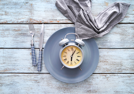 Grey alarm clock with plate on light wooden table