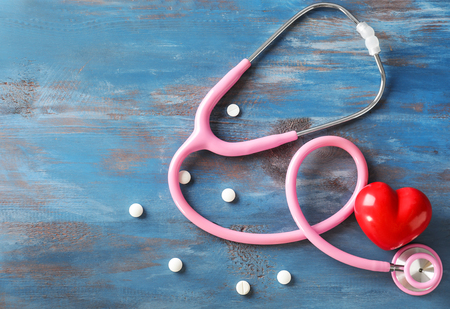 Medical stethoscope, red heart and pills on wooden background. Cardiology conceptの写真素材