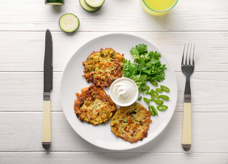 Plate with zucchini pancakes and sauce on light wooden tableの写真素材