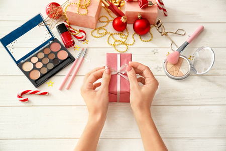 Woman with Christmas present and set of decorative cosmetics on white wooden backgroundの写真素材
