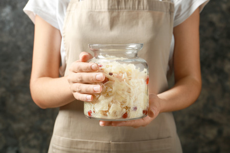 Woman holding glass jar with homemade sauerkraut on dark background, closeupの写真素材
