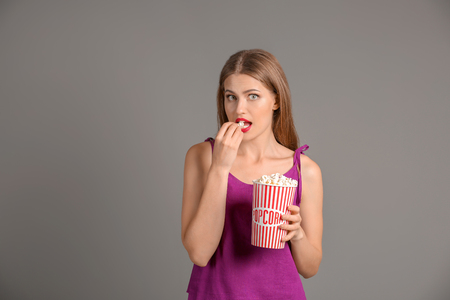 Beautiful young woman with cup of popcorn on grey backgroundの写真素材