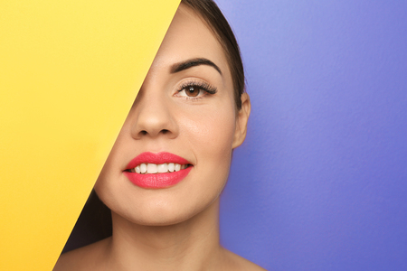 Beautiful young woman with bright lipstick and blank poster on color backgroundの写真素材