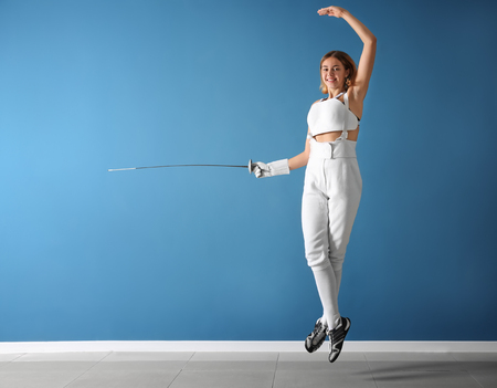 Young female fencer against color wall