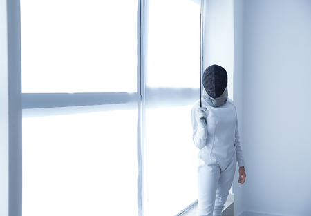 Young female fencer near window in gym