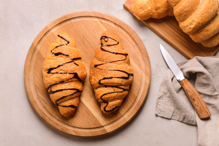 Board with tasty croissants and chocolate syrup on grey tableの写真素材