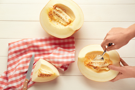 Woman taking seeds out of ripe sliced melon at white wooden tableの写真素材