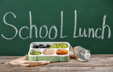 Lunch box with appetizing food and bottle of water on table in classroomの写真素材
