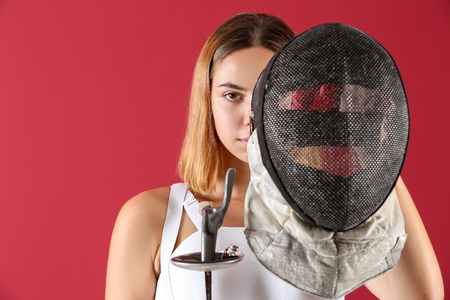 Young female fencer on color background