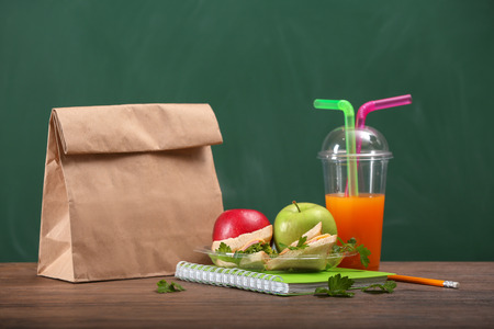 Plate with appetizing food for schoolchild and plastic cup of juice on wooden tableの写真素材