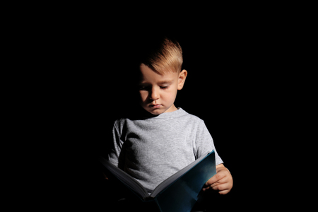 Cute little boy reading book on dark backgroundの写真素材