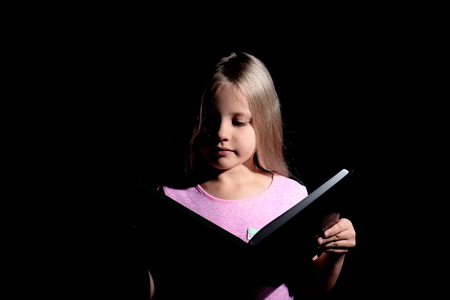 Cute little girl reading book on dark backgroundの写真素材