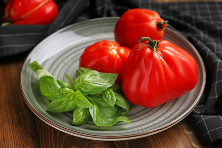 Plate with delicious tomatoes and fresh basil on wooden table, closeupの写真素材
