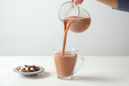 Woman pouring tasty cocoa from jug into cup on white tableの写真素材