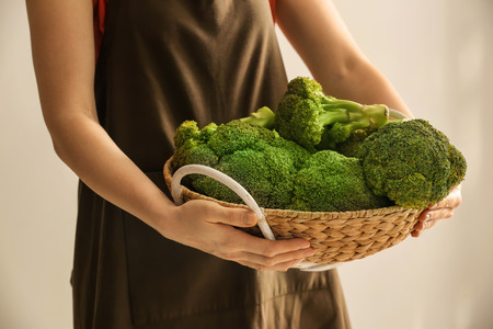 Woman holding basket with fresh green broccoli on light background, closeupの写真素材