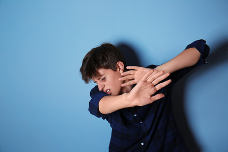Scared teenage boy trying to protect himself with hands on color background. Bullying at schoolの写真素材