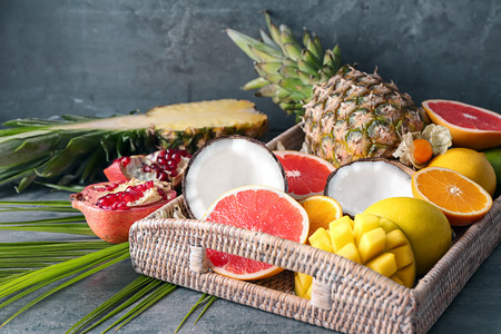 Wicker tray with various delicious fruits on grey tableの写真素材