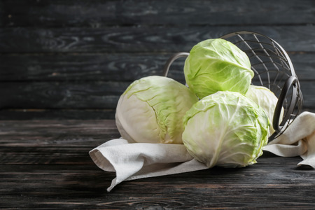 Overturned metal basket with fresh cabbages on wooden tableの写真素材