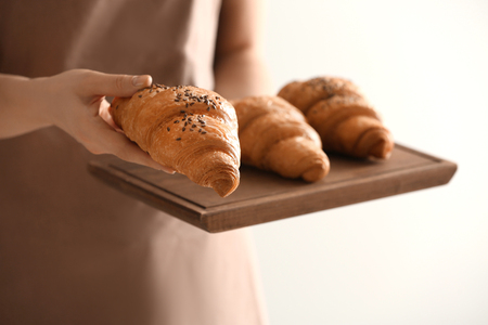 Young woman holding wooden board with tasty croissants on light backgroundの写真素材