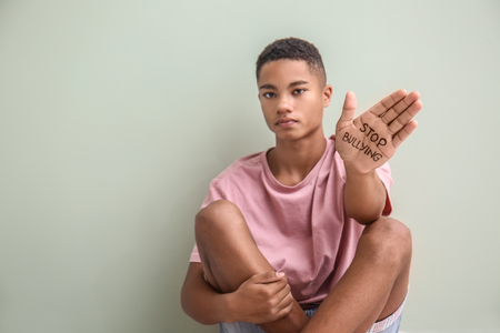 African-American teenage boy with text STOP BULLYING written on hand near light wallの写真素材