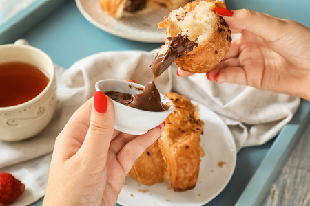 Woman eating tasty croissant with chocolate paste, closeup