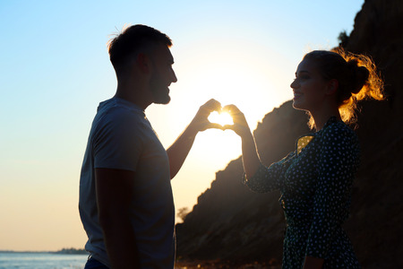 Cute young couple making heart with their hands on sea shoreの写真素材