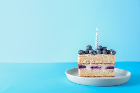Piece of delicious birthday cake with burning candle on color backgroundの写真素材