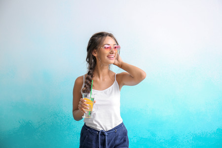 Young woman with glass of fresh lemonade on color background