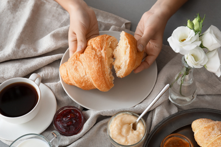 Woman eating tasty croissant with cream on tableの写真素材