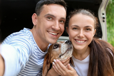 Young couple with cute dog taking selfie near car outdoorsの写真素材