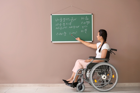 Female teacher in wheelchair near chalkboard at schoolの写真素材