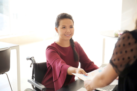 Asian woman in wheelchair working with colleague in officeの写真素材