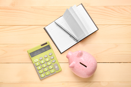 Cute piggy bank with notebook and calculator on wooden tableの写真素材