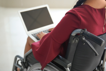 Asian woman in wheelchair working with laptop in office