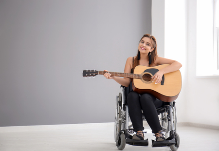 Beautiful young musician in wheelchair playing guitar indoorsの写真素材