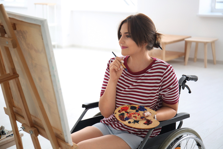 Young female artist in wheelchair painting picture at homeの写真素材