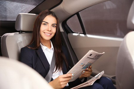 Young businesswoman reading newspaper in car