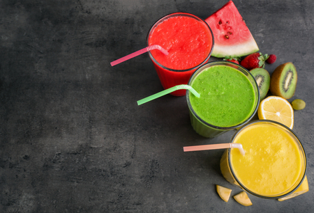 Glasses of tasty smoothies with fruits on grey tableの写真素材