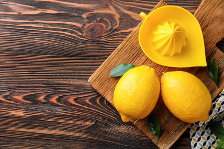 Whole ripe lemons and juicer on wooden tableの写真素材