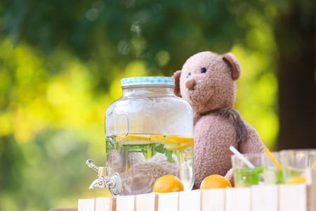 Bear toy with glass jar dispenser of natural lemonade on stand in parkの写真素材