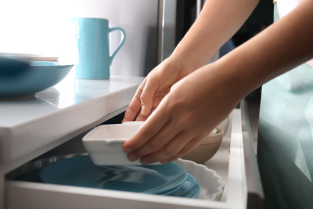 Woman putting ceramic dish into kitchen drawerの写真素材