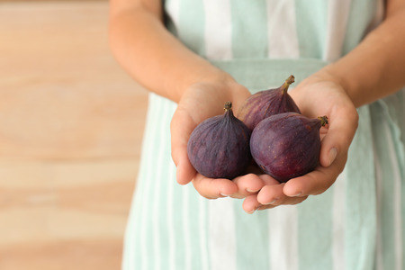 Woman holding fresh ripe figs on wooden background, closeup