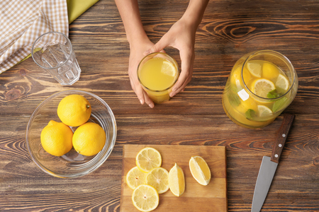 Woman holding glass of fresh lemon juice on wooden backgroundの写真素材