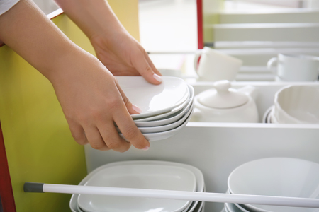 Woman putting plates into kitchen drawerの写真素材